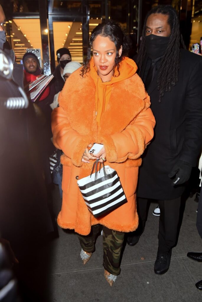 Rihanna en pantalon cargo militaire, sweat à capuche orange, manteau de la même couleur et escarpins