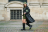 Femme en ensemble vert olive, manteau long en cuir noir et bottes noires