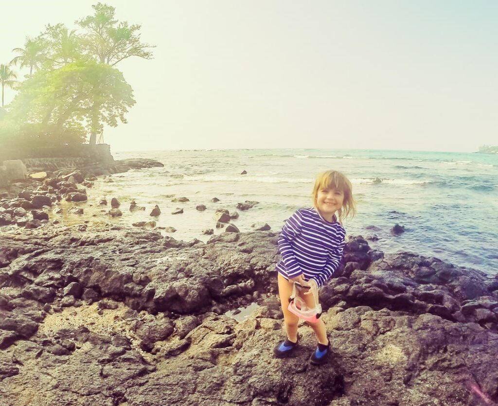 Enfant sur une plage pierreuse portant des chaussures d'eau