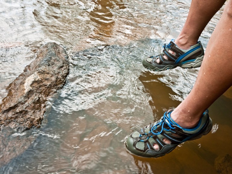 Homme assis au bord d'une mer au fond pierreux portant des chaussures d'eau